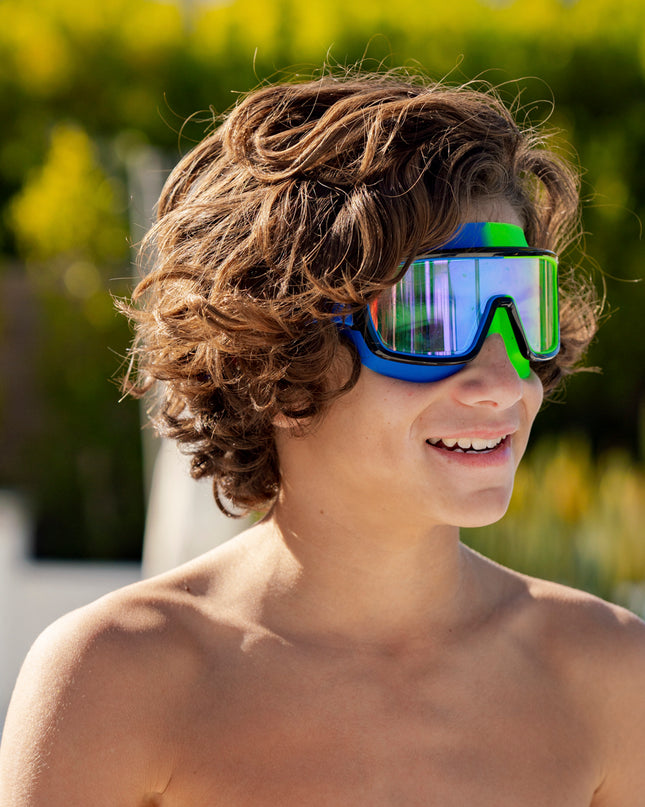 boy smiling poolside wearing prismatic swim goggles in cyborg cyan showing wide frame, neon colored gasket and mirrored lens