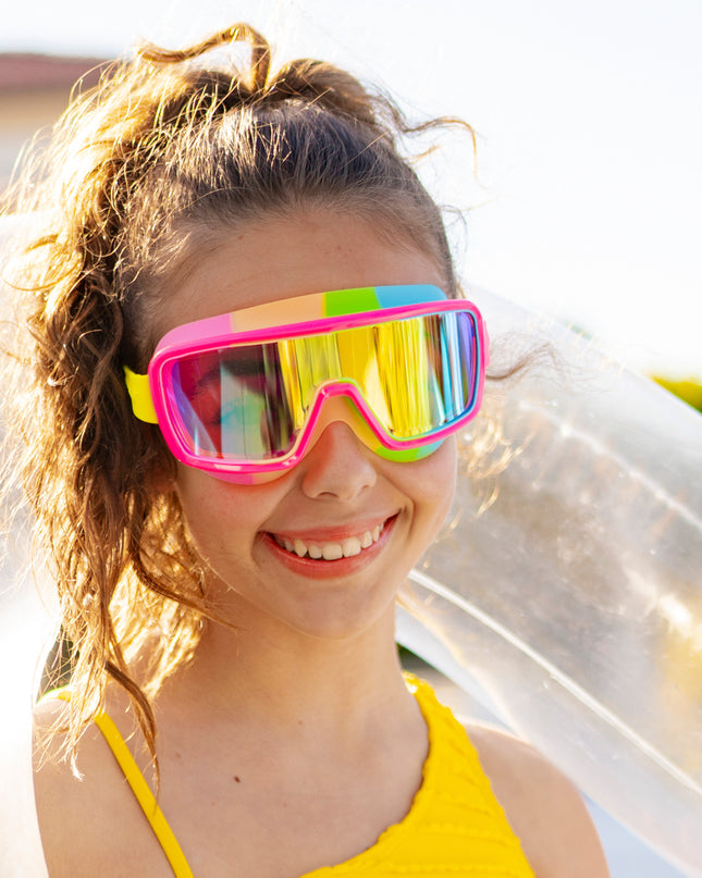 girl smiling poolside wearing chromatic swim goggles in spectro strawberry showing a hot pink frame and rainbow colored gasket with reflective lens