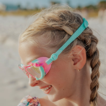 girl at beach looking down wearing mystical mermaid kids' swim goggles showing 3d mermaid detail and rhinestones and fishtail textured strap