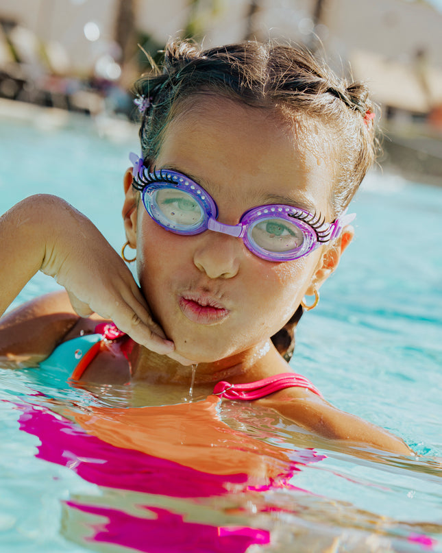 girl in swimming pool posing wearing splash lash kids' swim goggles in purple polish showing faux lashes and rhinestones