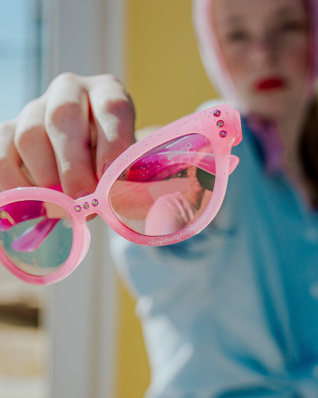 girl holding malibu beach kid's sunglasses in pisces pink to camera showing pink glitter frame and pink rhinestone detail