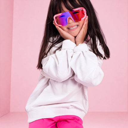 girl smiling in pink studio wearing pink sand kids sunglasses in the color sprinkle pink 