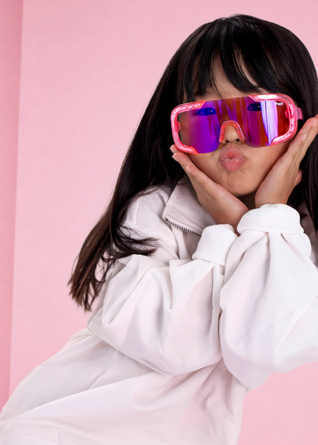 girl posing in pink studio wearing pink sand kids sunglasses in the color sprinkle pink 