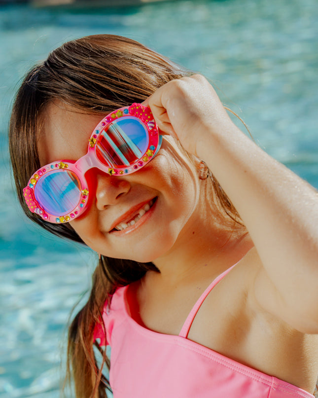 lifestyle of girl in front of pool smiling wearing candy carnival kids swim goggles showing rhinestones and cotton candy detail