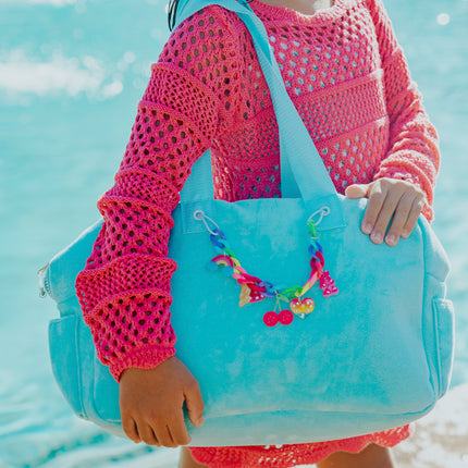 Lifestyle of child holding blue crush velour tote at beach showing rainbow chain with charms