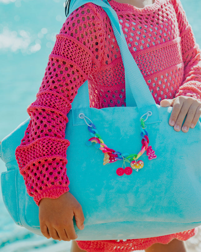 Lifestyle of child holding blue crush velour tote at beach showing rainbow chain with charms