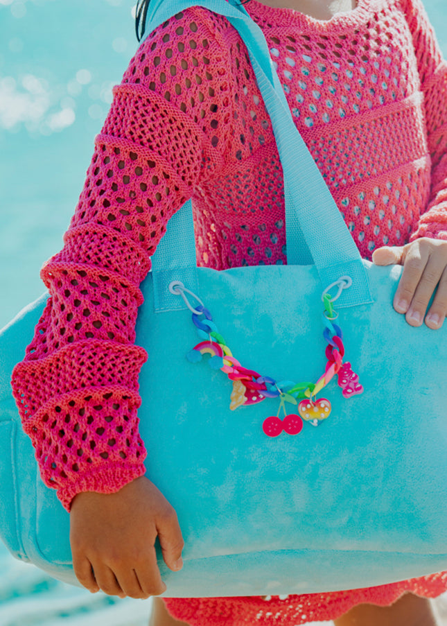 Lifestyle of child holding blue crush velour tote at beach showing rainbow chain with charms
