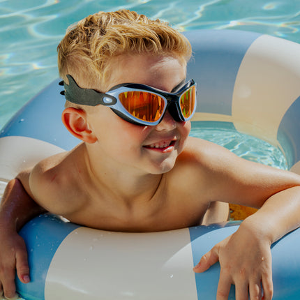 lifestyle of child swimming in pool wearing covert chomp swim goggles showing red lens and shark tooth screen printed lens