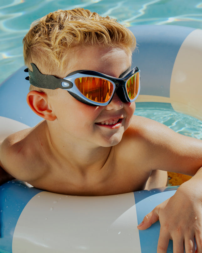 lifestyle of child swimming in pool wearing covert chomp swim goggles showing red lens and shark tooth screen printed lens