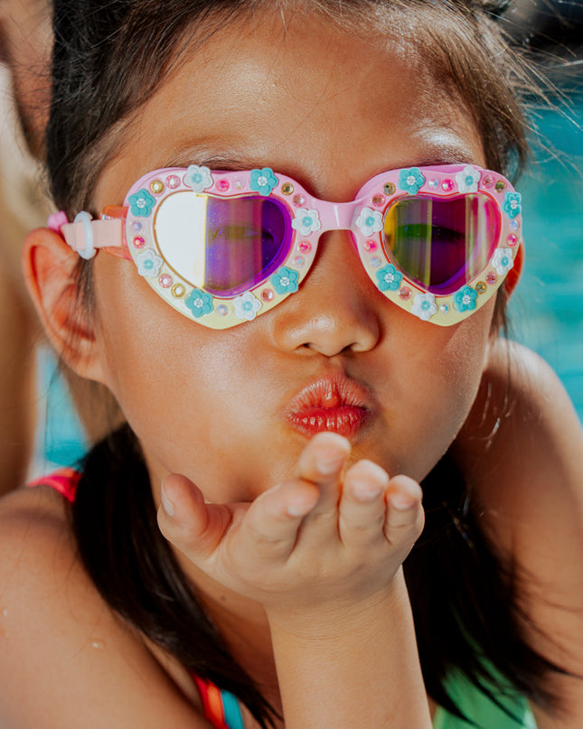 lifestyle of girl playfully blowing kiss poolside wearing daisies at dawn heart shaped swim goggles