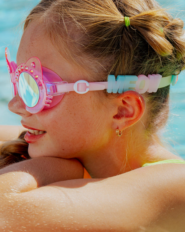 lifestyle image of girl poolside looking away wearing frosted feline swim goggles in pink purr showing silicone sliders spelling MEOW
