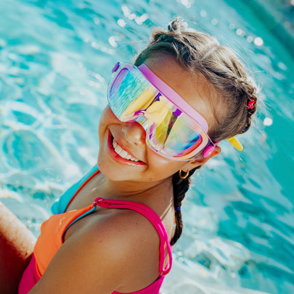 lifestyle of girl sitting poolside wearing hologlow swim goggles in bubblegum beam pink showing reflective lens