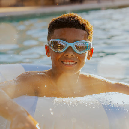 lifestyle of boy swimming in inner tube wearing jawsome kids swim goggles in baby blue tip showing shark tooth printed lens