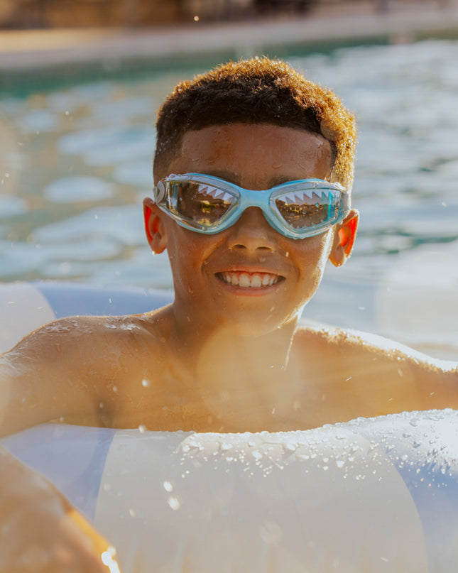 lifestyle of boy swimming in inner tube wearing jawsome kids swim goggles in baby blue tip showing shark tooth printed lens