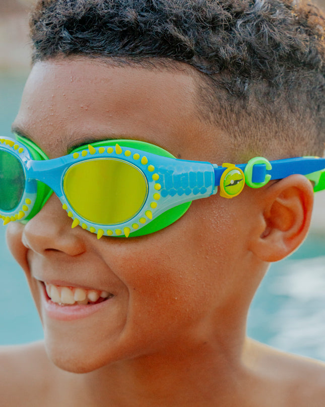 lifestyle of kid smiling wearing jurassic dive swim goggles in stego splash green showing silicone spike details and reptilian printed lens with eye ball slider detail