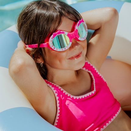 lifestyle image of girl wearing ribbon glam kids swim goggles laying in inflatable inner tube