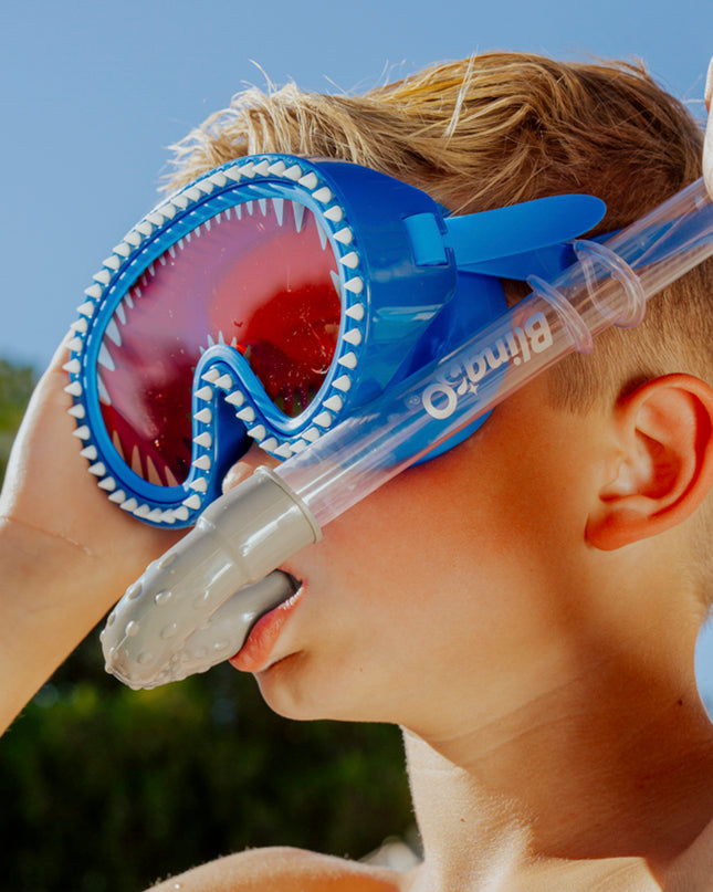 angled view of boy wearing shark attack kids swim mask showing silicone spike details and red lens while using shark bite shark fin snorkel in blue grey 