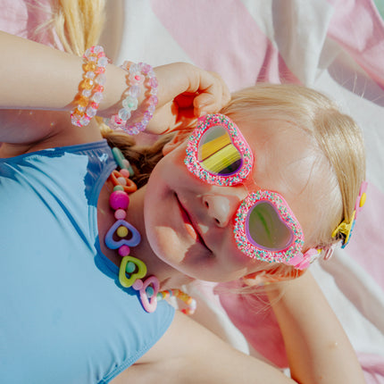lifestyle image of child laying on beach towel wearing sprinkle heart kid's swim goggles 