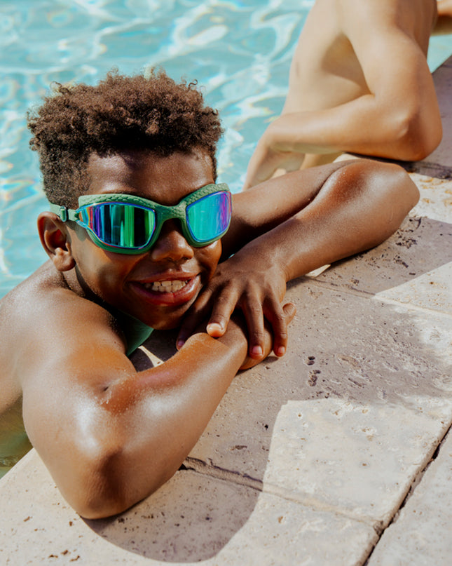 kid hanging out pool side wearing streamline swim goggles in current green showing the textured silicone frame