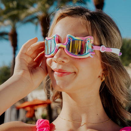 girl smiling standing in front of palm trees wearing tie-dye tabby all silicone cat shaped swim goggles in meowberry breeze 