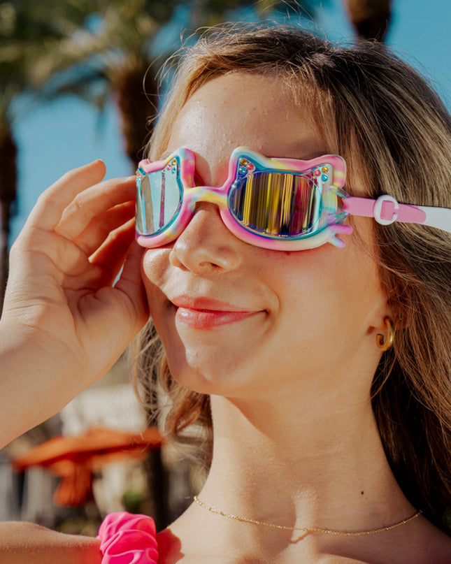 girl smiling standing in front of palm trees wearing tie-dye tabby all silicone cat shaped swim goggles in meowberry breeze 