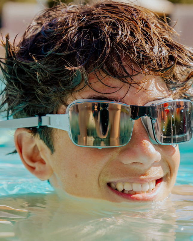 teen boy swimming and smiling while wearing velocity swim goggles in onyx showing frameless black lens and tan silicone strap