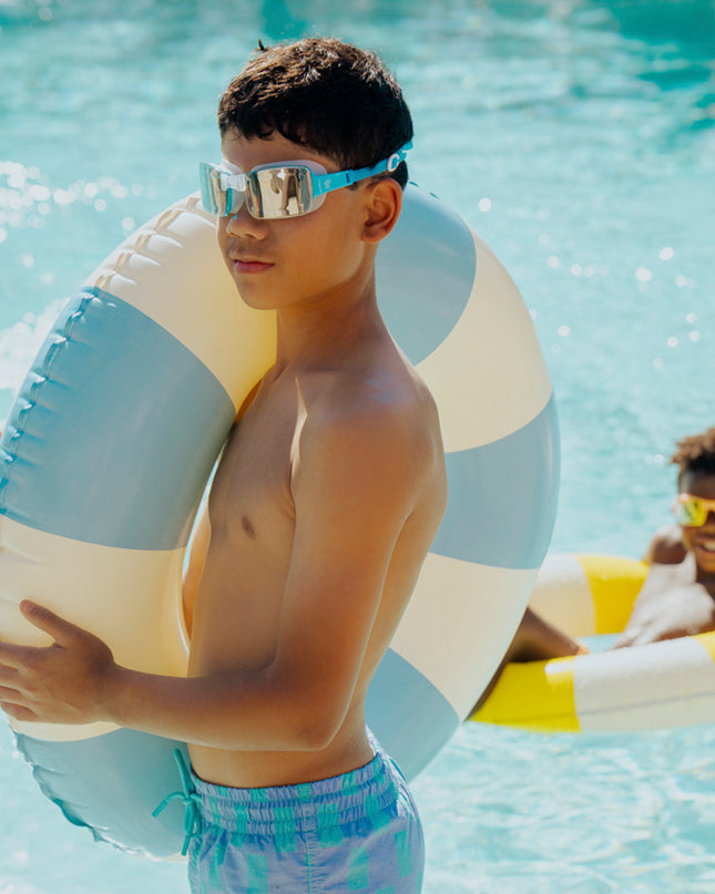 junior boy standing poolside wearing velocity swim goggles in wave blue showing frameless lens and blue silicone strap