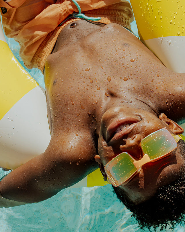 boy swimming relaxing in inner tube wearing velocity swim goggles in volt showing gold colored frameless lens