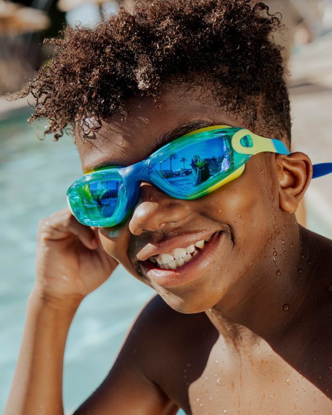 boy sitting poolside smiling wearing voyage swim goggles in rainforest showing reflective lens and silicone frame